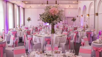 A banquet hall with round tables, pink and white tablecloths, and chairs with pink sashes.