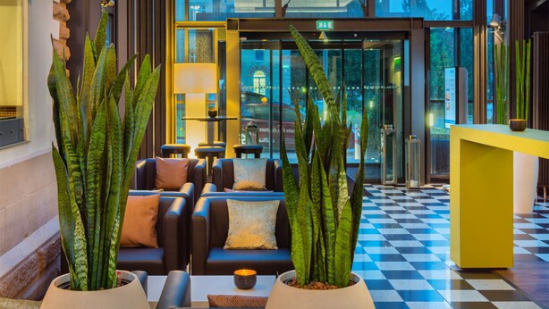A lobby with a checkered floor, sofas, potted plants, and a reception desk.