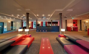 Un hall modern amb taulell d'informació, zona de seients i finestrals grans.