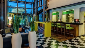 A modern lobby with a checkered floor, a bar area with green bar stools, and large potted plants.