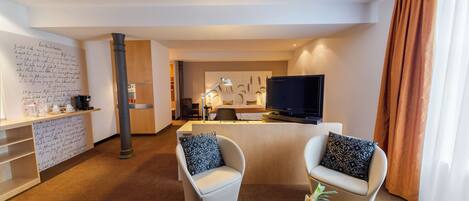 A hotel room with a dining area, a TV, and a desk with a lamp.