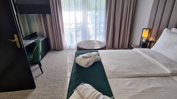A hotel room with a bed, a TV, a desk, a chair, a lamp, and a view of the outdoors.