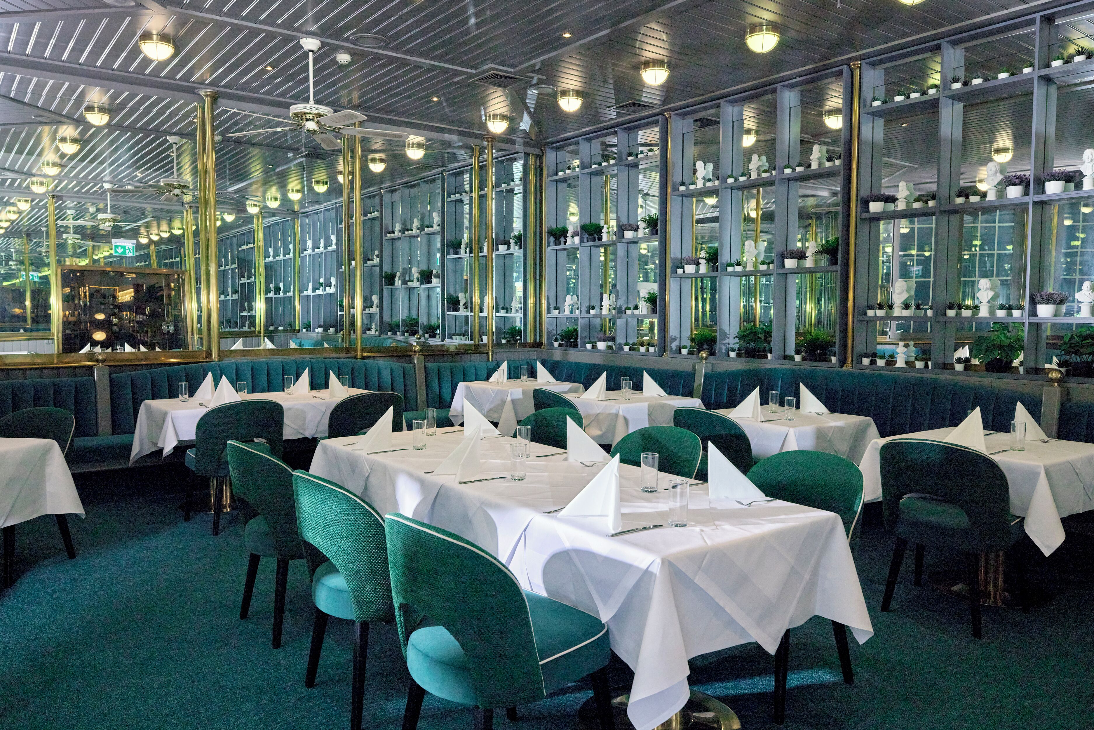 A restaurant with multiple tables and booths, large windows, and a ceiling with reflective panels.