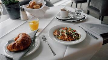 A breakfast setting with croissants, a plate of food, a glass of orange juice, and a cup of coffee on a table.