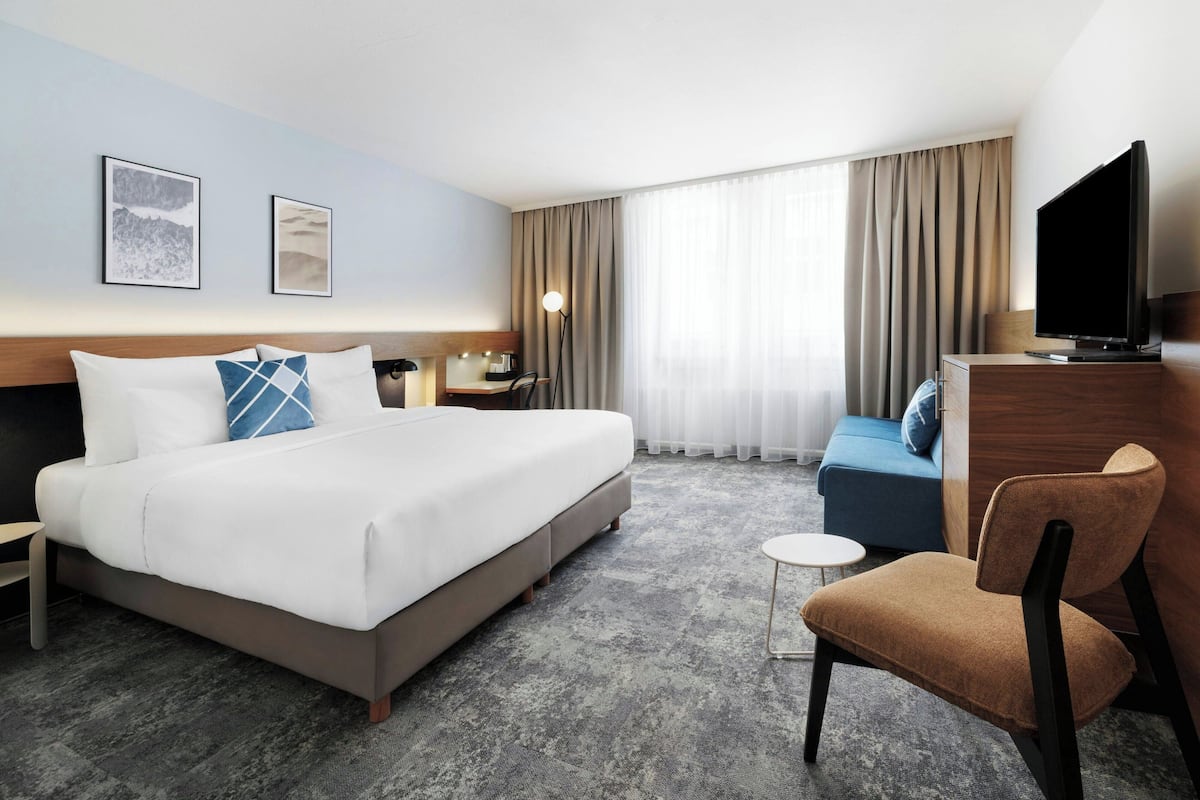A hotel room with a large bed, a sofa, a chair, a desk, a television, and two framed pictures on the wall.