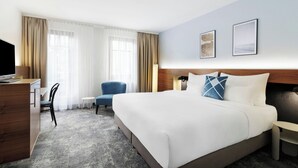 Ein Hotelzimmer mit Bett, Schreibtisch, Stuhl, kleinem Tisch und Fernseher.