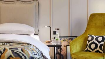 Ein modernes Hotelzimmer mit einem Bett, einem Nachttisch mit Lampe, einem Sessel und einem gerahmten Bild an der Wand.