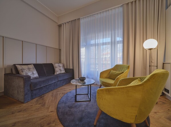 Una sala de estar moderna con un sofá gris oscuro, dos sillones amarillos, una mesa redonda de centro y una lámpara de pie.