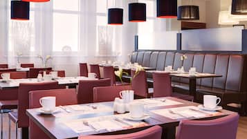 A modern restaurant with red leather booths and tables, black pendant lights, and white table settings.
