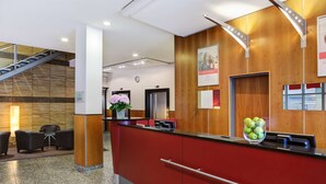 Un espace d’accueil avec un comptoir rouge, un escalier et une horloge au mur.