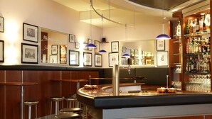 Un espace bar avec des tabourets, un comptoir, des tableaux encadrés au mur et une étagère remplie de bouteilles.
