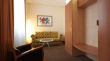 A hotel room with a checkered sofa, a small round table, a lamp, and a painting on the wall.