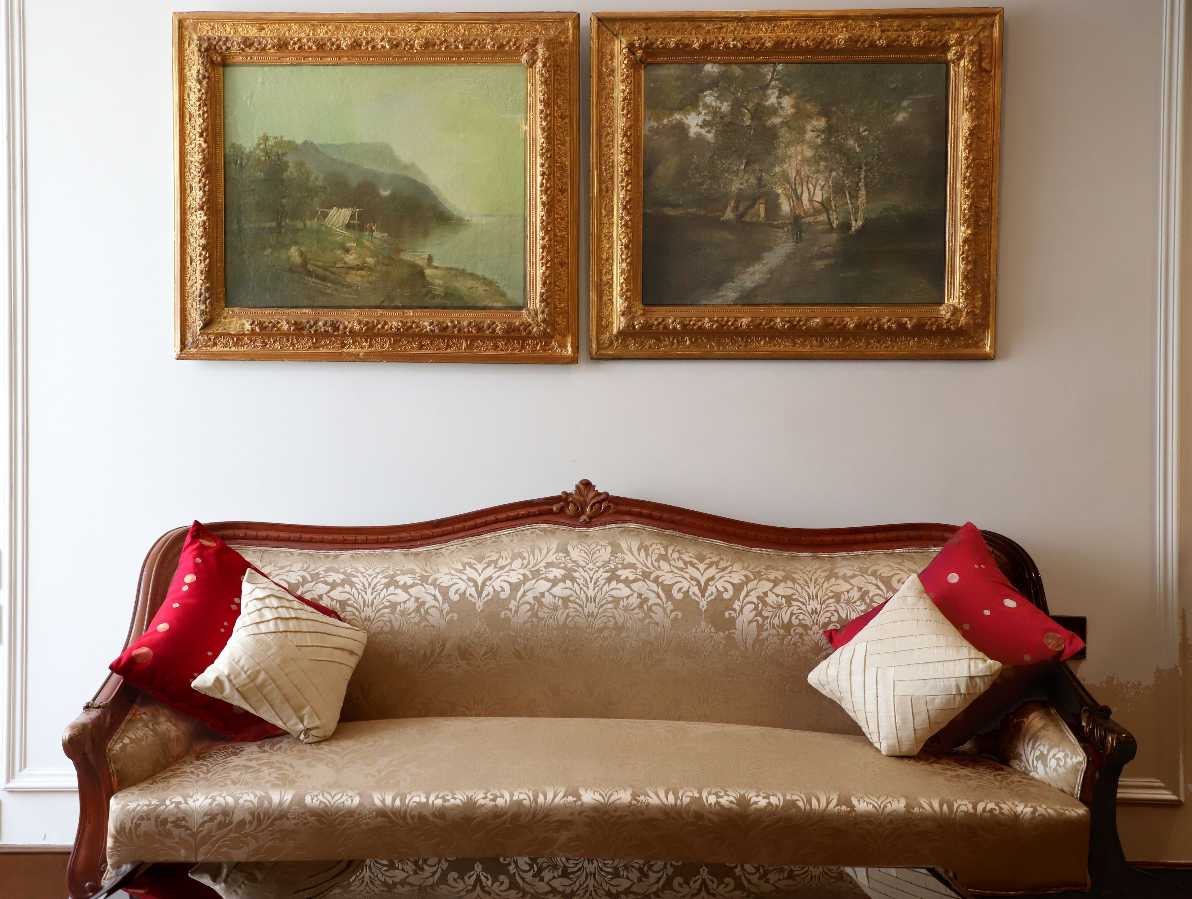 A room with a classic sofa and two framed paintings on the wall.