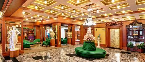 A luxurious lobby with marble flooring, ornate ceiling, and green seating areas.