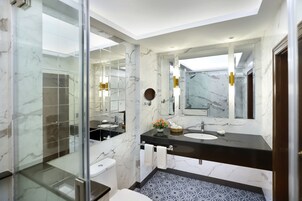A modern bathroom with a glass shower enclosure, a marble-tiled floor, a black countertop sink, and a large mirror.