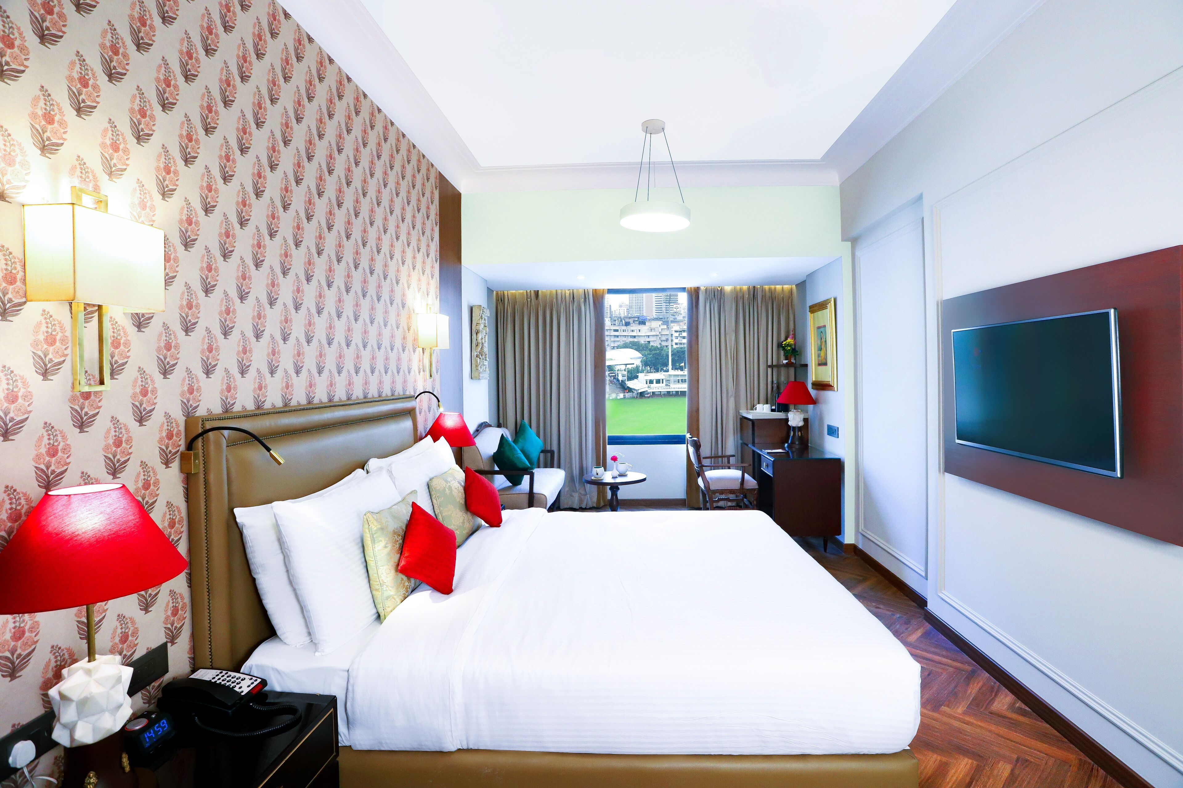A hotel room with a large bed, a desk with a chair, a TV, and a view of the city through the window.