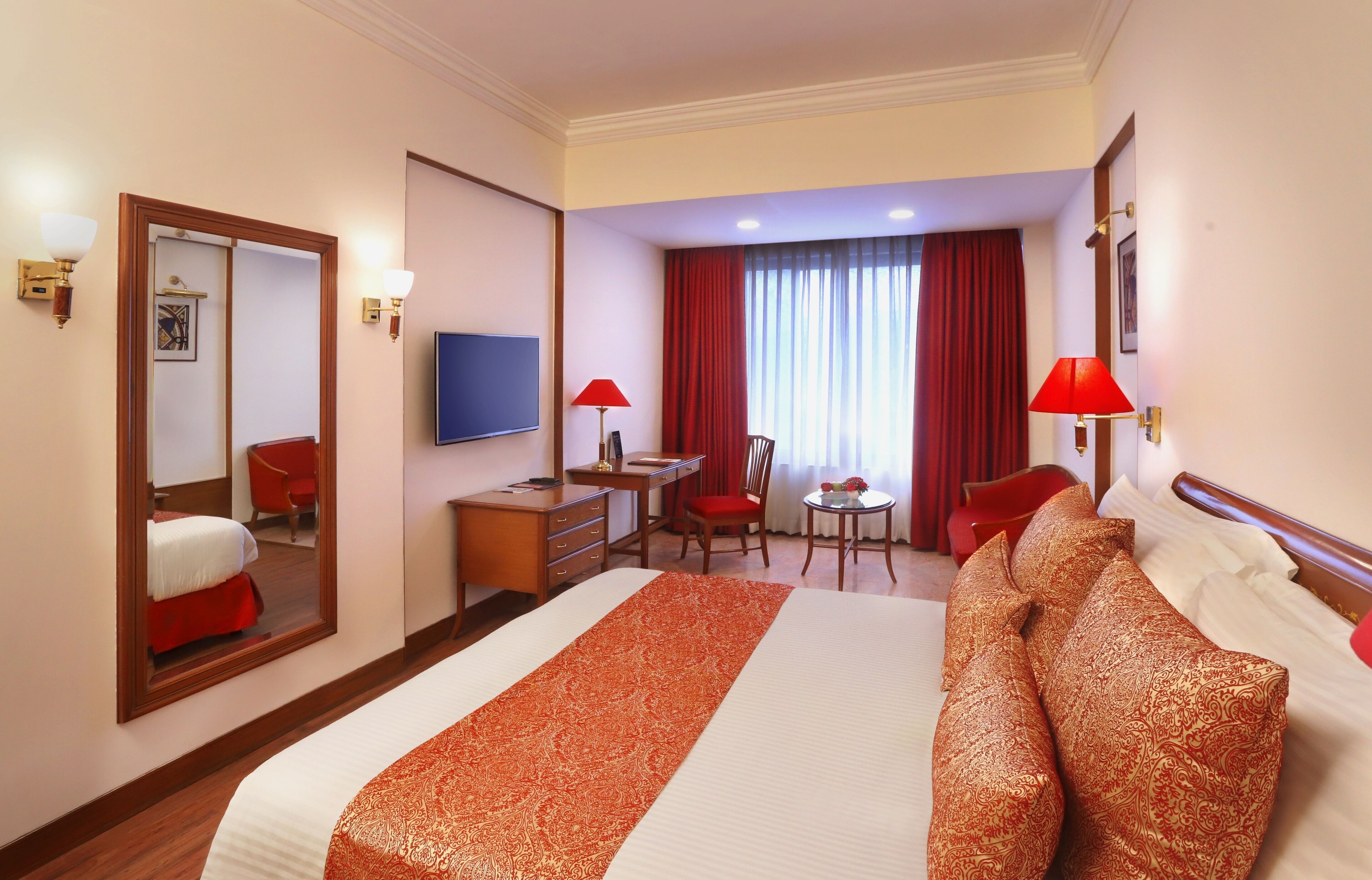 Quarto de hotel com uma cama grande, uma escrivaninha, uma cadeira, uma mesinha e uma televisão.