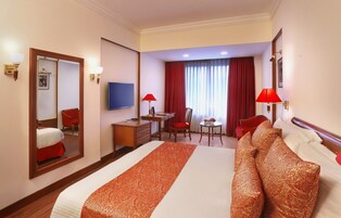 A hotel room with a large bed, a desk, a chair, a small table, and a TV.