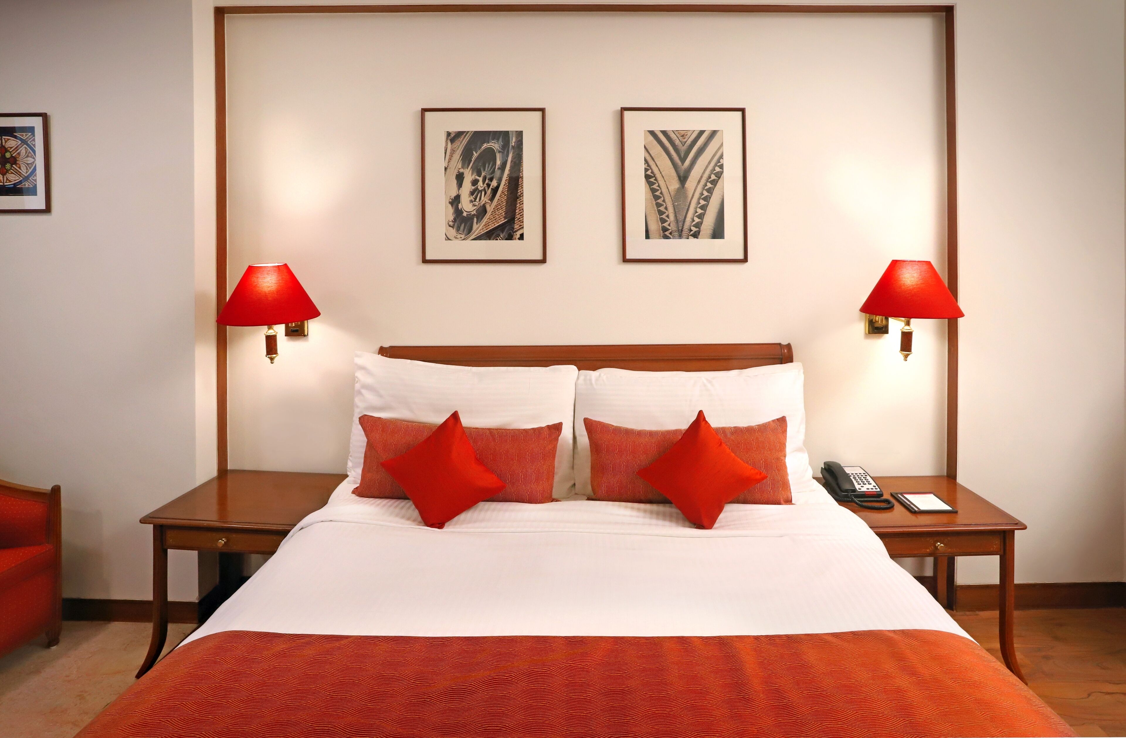 Een hotelkamer met een groot bed, twee rode lampen, een telefoon en twee ingelijste foto's aan de muur.