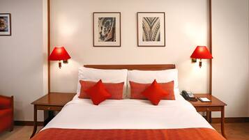 Een hotelkamer met een groot bed, twee rode lampen, een telefoon en twee ingelijste foto's aan de muur.