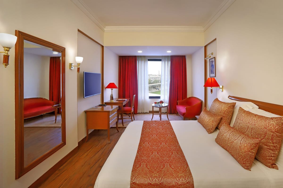 Habitación de hotel con una cama grande, un escritorio, una silla, un televisor y vistas a un paisaje urbano.