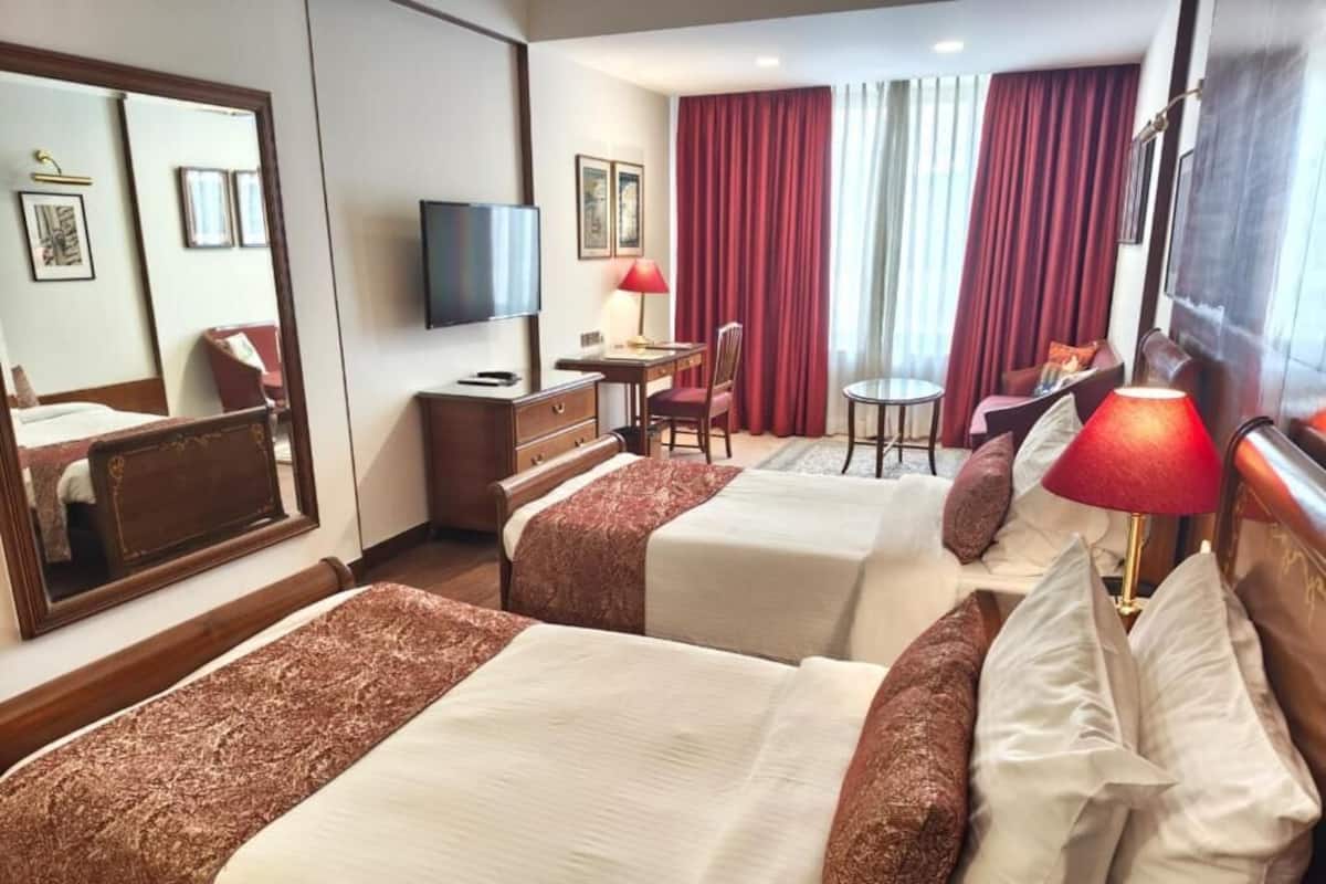 Habitación de hotel con dos camas, un escritorio, una silla, un televisor y una ventana con cortinas.