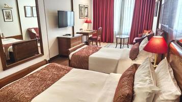 A hotel room with two beds, a desk, a chair, a TV, and a window with curtains.