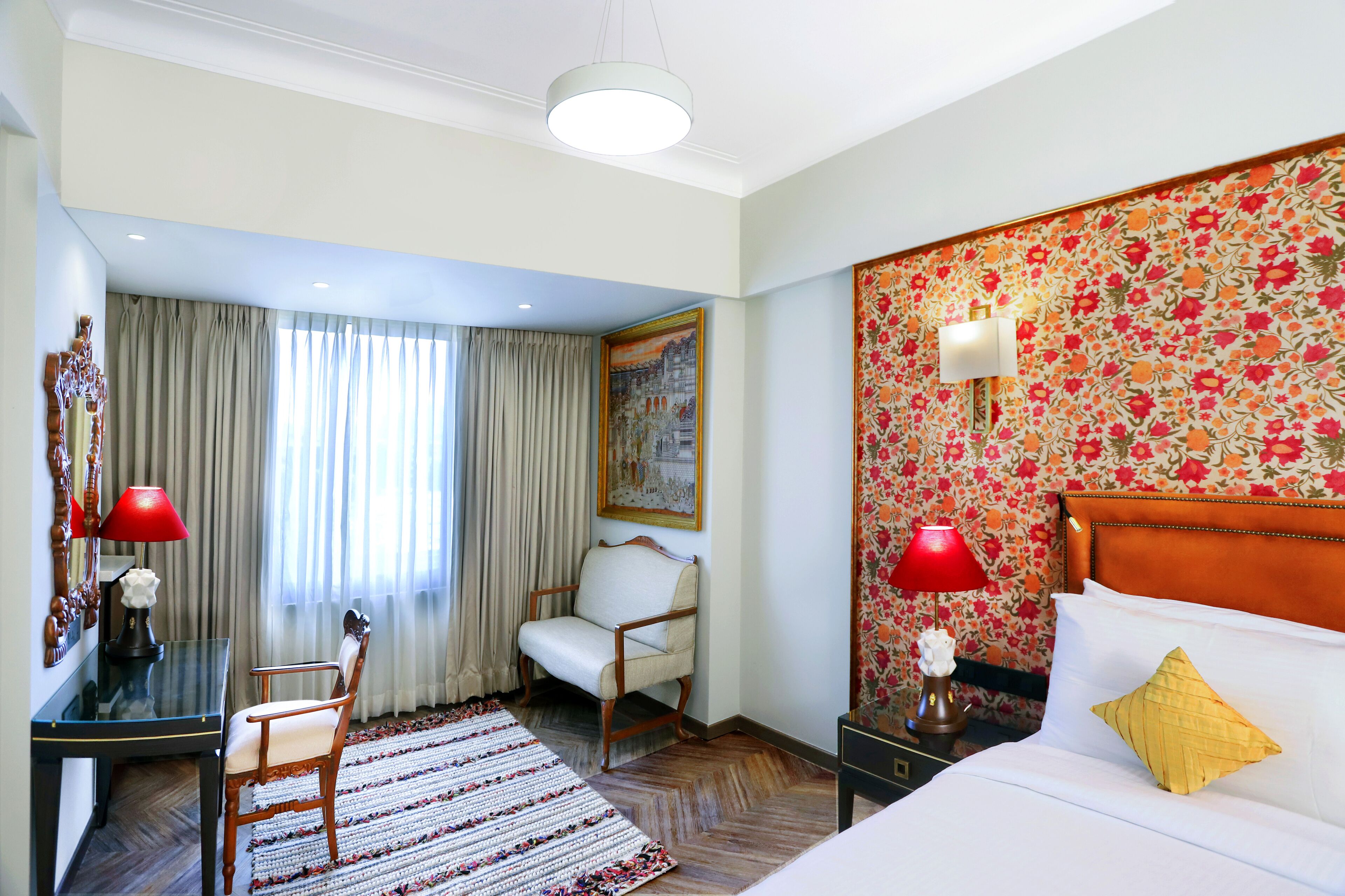 Habitación de hotel con una cama, un escritorio, una silla, una alfombra y un cuadro en la pared.