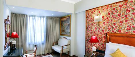 Habitación de hotel con una cama, un escritorio, una silla, una alfombra y un cuadro en la pared.