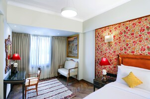 Habitación de hotel con una cama, un escritorio, una silla, una alfombra y un cuadro en la pared.
