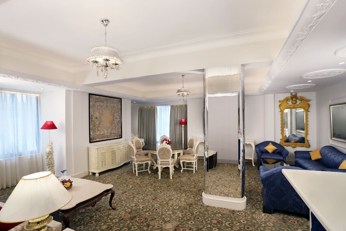 Una habitación de hotel con comedor, sofá, televisor y un espejo grande.