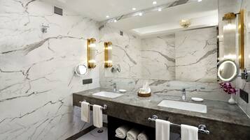 Un baño moderno con paredes de mármol, dos lavamanos, un espejo grande y un mueble de tocador con toallas.