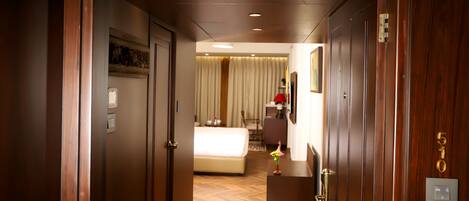 A hotel hallway with wooden doors, a bed with white bedding, a desk with a vase, and a number 510 sign.