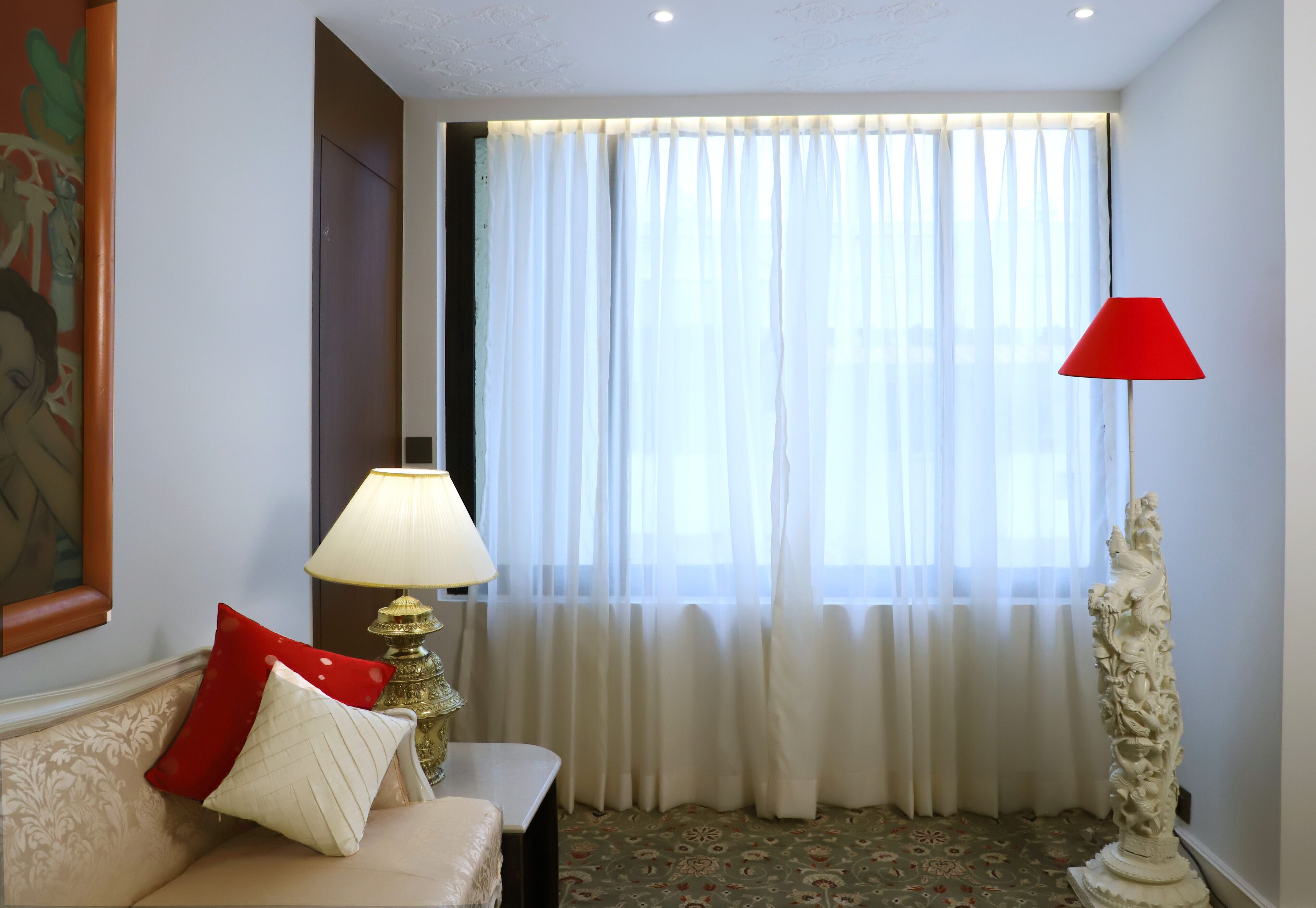 A room with a sofa, a lamp, a red floor lamp, and a decorative column.