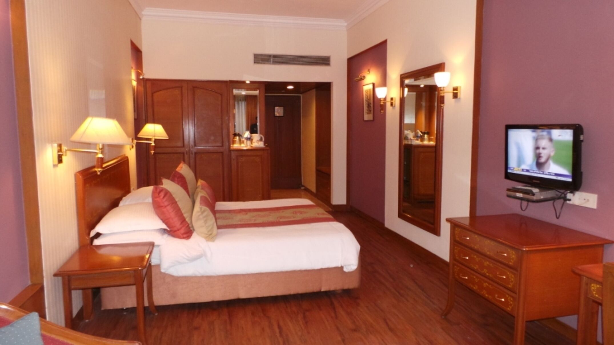A hotel room with a bed, bedside lamps, a television, a dresser, and a mirror.