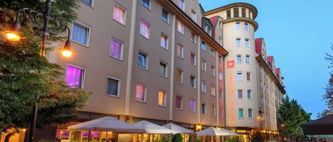 A hotel with multiple floors, outdoor seating with umbrellas, and a prominent building name.