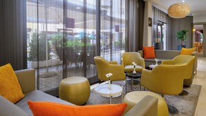A modern hotel lobby with yellow and grey seating, large windows, and a view of the street. - Leonardo Hotel Budapest (Budapest)