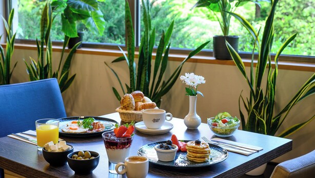 A breakfast table with various food items, a coffee cup, and a vase with flowers. - Leonardo Hotel Budapest (Budapest)