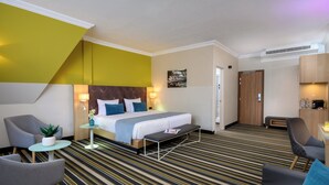 A hotel room with a bed, two armchairs, a small table with a plant, and a bench. - Leonardo Hotel Budapest (Budapest)