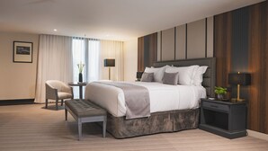 A modern hotel room with a large bed, a bedside table, a chair, and a small table with a vase. - Lidotel Caracas (Caracas)