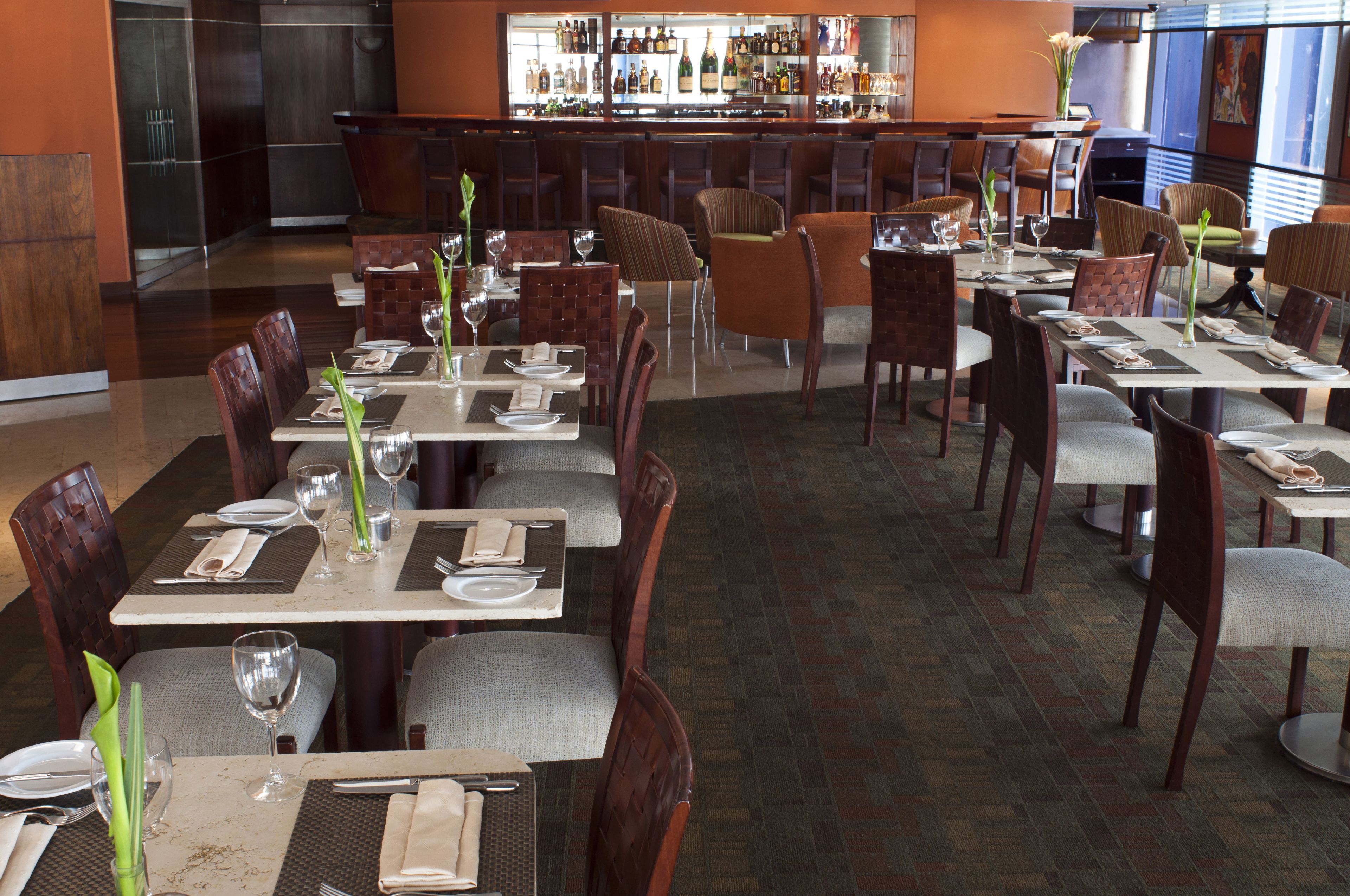 Un ristorante con diversi tavoli e sedie, un'area bar sullo sfondo e un pavimento tappezzato.