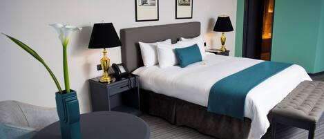 A hotel room with a large bed, bedside tables, a round table, and a bench.