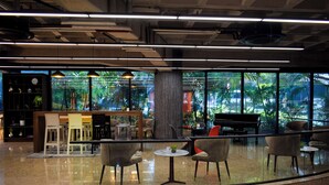 A modern indoor space with a bar area, seating, and large windows offering a view of greenery. - Lidotel Caracas (Caracas)