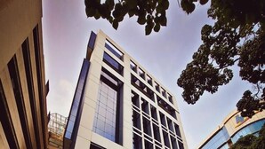 A modern building with a glass facade, a covered entrance, and a landscaped area with parked cars. - Lidotel Caracas (Caracas)
