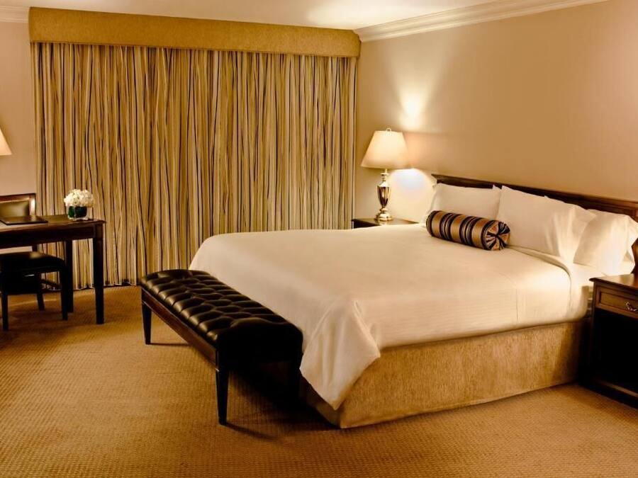 Habitación de hotel con una cama grande, dos mesitas de noche con lámparas, un escritorio con silla y un banco.