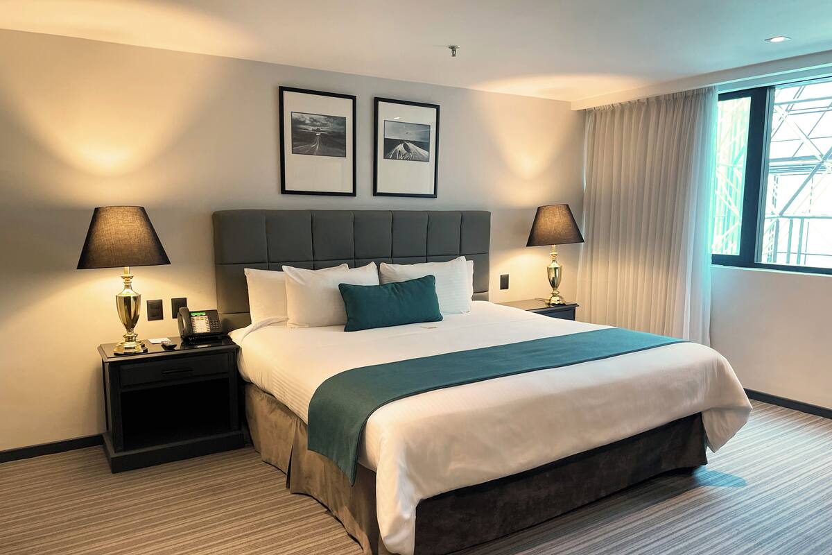 Ein Hotelzimmer mit einem großen Bett, zwei Nachttischen mit Lampen, einem Kopfteil und zwei gerahmten Bildern an der Wand.
