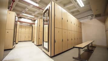 A locker room with multiple wooden lockers, a bench, and fluorescent lighting.