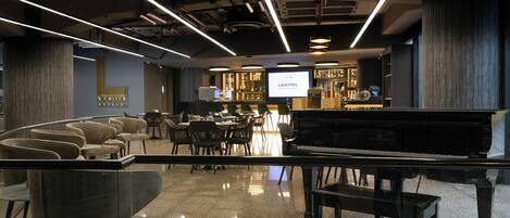 A modern hotel lobby with a piano, seating area, and a bar.