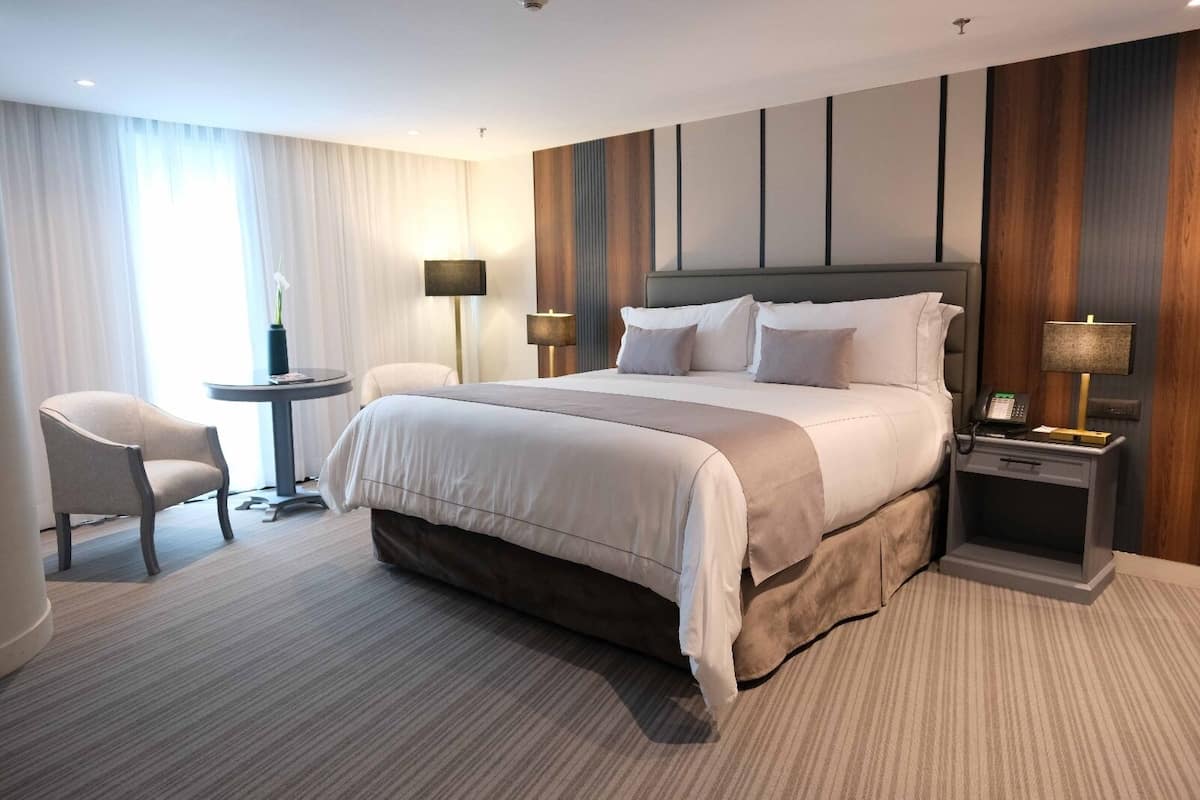 Ein Hotelzimmer mit einem großen Bett, Nachttischen, einem Sessel und einer Lampe.