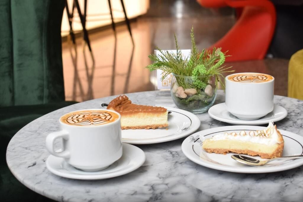 Ein Tisch mit einer weißen Tasse Kaffee, einem Stück Käsekuchen und einer kleinen Topfpflanze.